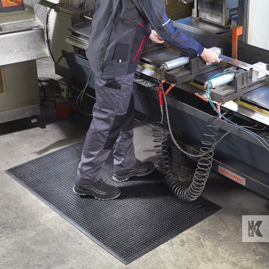 Kleen-Cushion - A man works at an industrial machine wearing overalls, he stands on a rubber mat for comfort and protection
