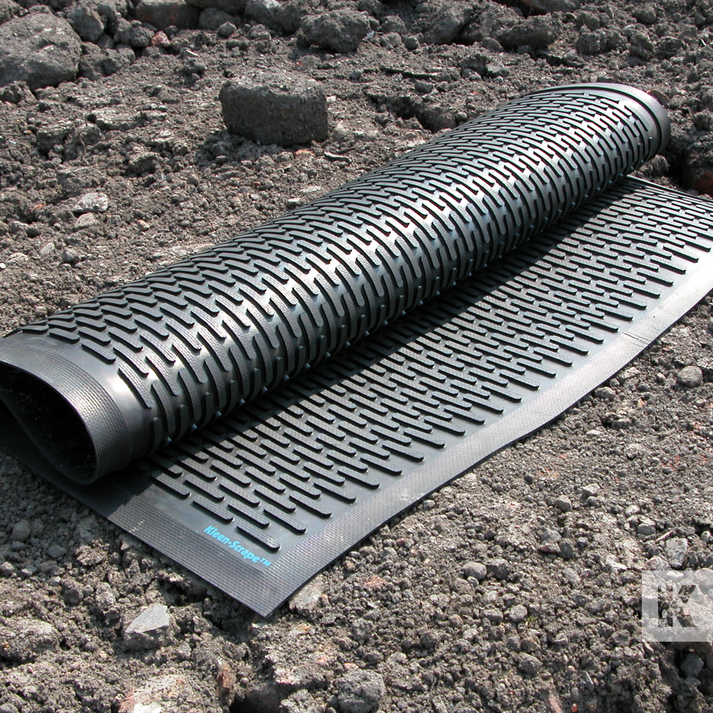 Kleen-Scrape - Heavy duty rubber mat, rolled up and displayed outdoors on some rough dirt terrain